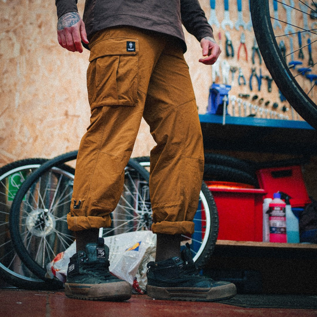 Person wearing brown pants standing in a workshop with bicycles and tools in the background